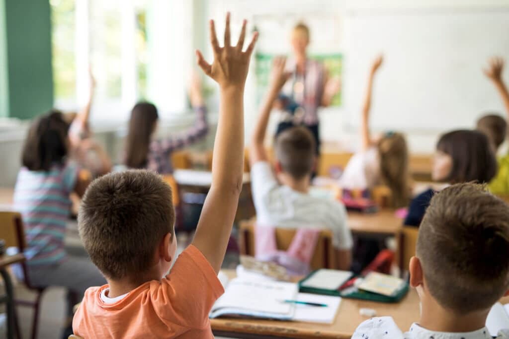 young students classroom, hands raised