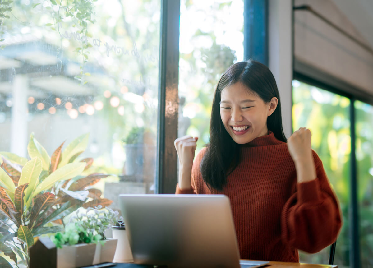 happy female finding unclaimed property on laptop, next to window and garden